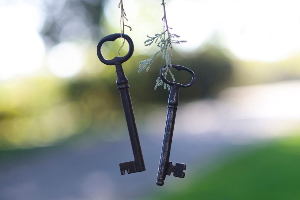 Legal tips for couples purchasing a home: two keys hang in the front of the frame in focus, with a driveway and garden out of focus in the background